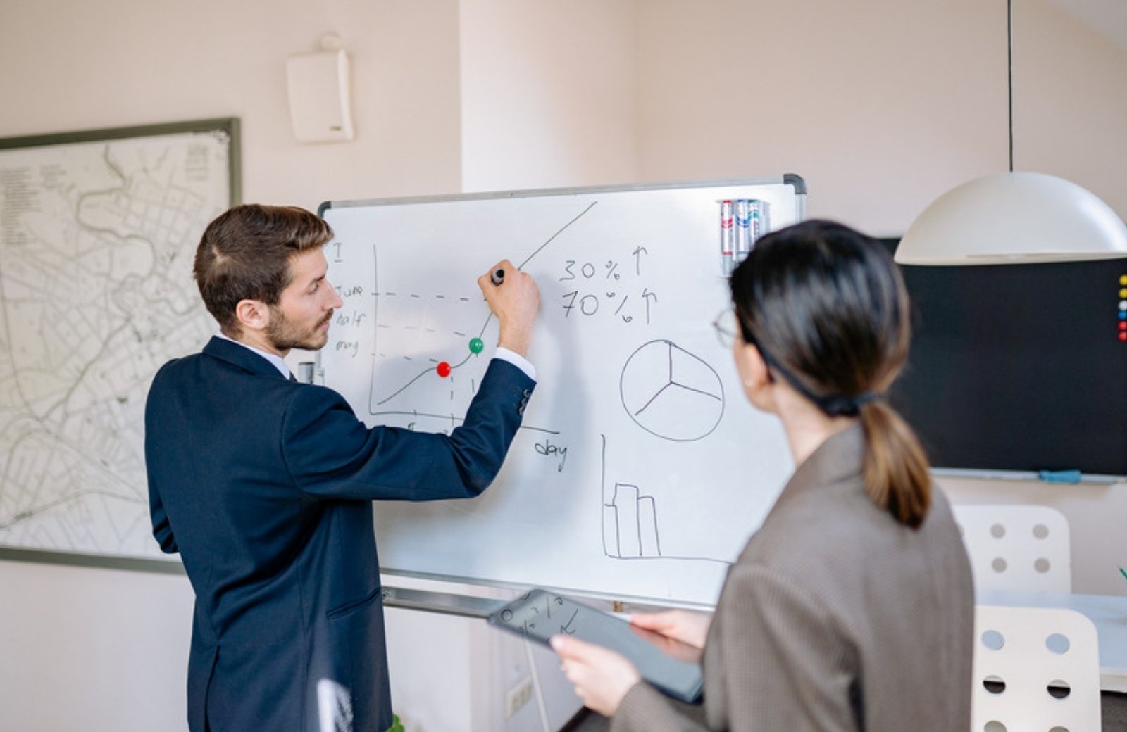 Marketer sketching a strategy on a whiteboard for a colleague