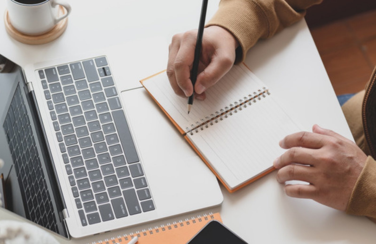 Person writing brand voice notes in a notebook next to a laptop